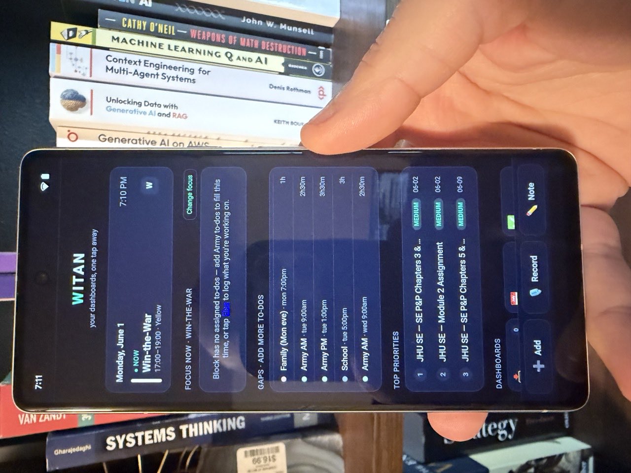 The Witan mobile dashboard, held in hand in front of a bookshelf